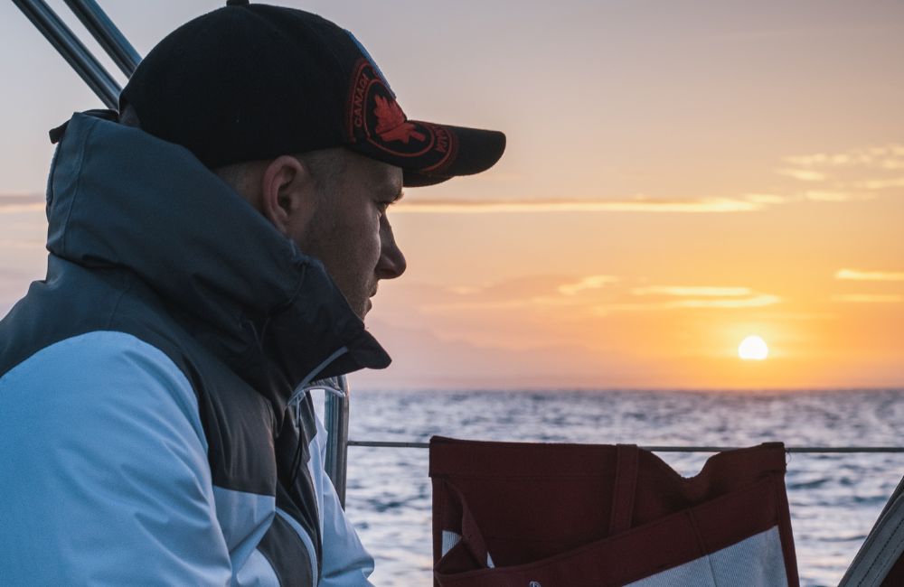 Foto di un ragazzo che osserva l'alba in barca a vela per il ponte del 25 aprile